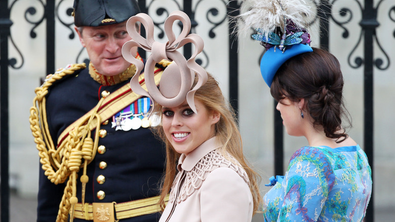 Princes Beatrice smiling with big bow hat on her head with Princess Eugenie standing next to her