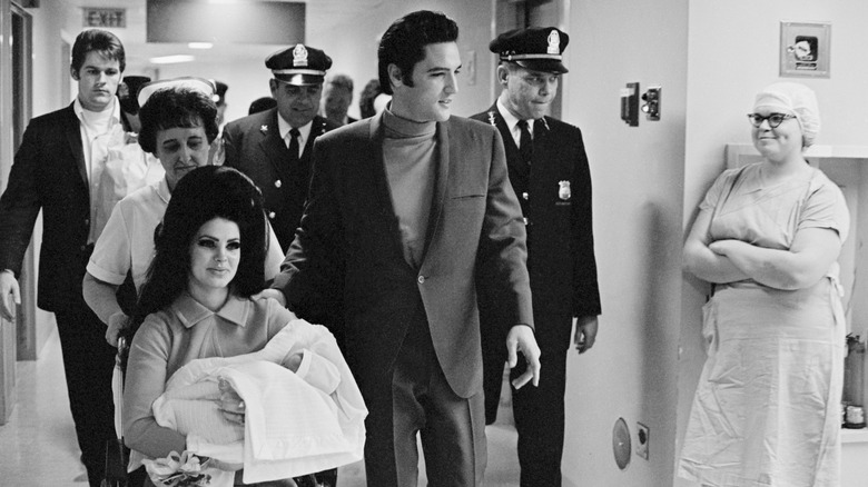(l-r): Priscilla Presley holding Lisa Marie Presley while sitting in a wheelchair next to Elvis Presley