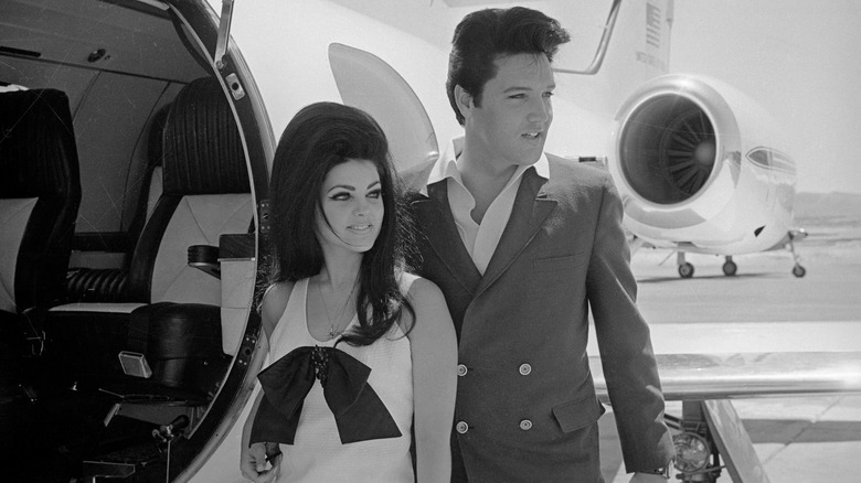 (l-r): Priscilla Presley and Elvis Presley posing next to his jet