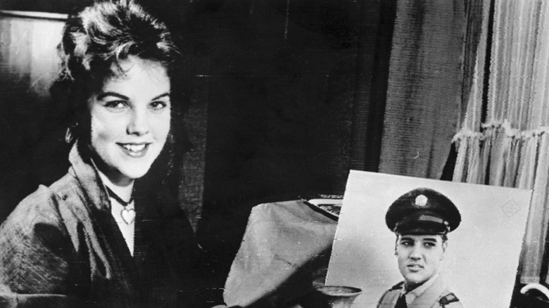 Priscilla Presley posing next to a photo of Elvis Presley.