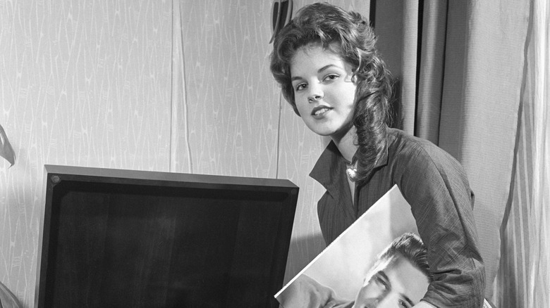Priscilla Presley looking at the camera while holding an Elvis album.