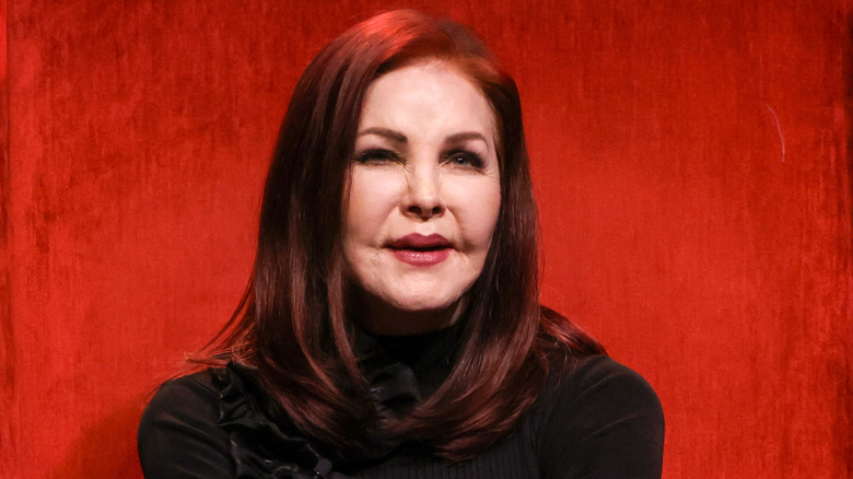 Priscilla Presley smiling against a red background