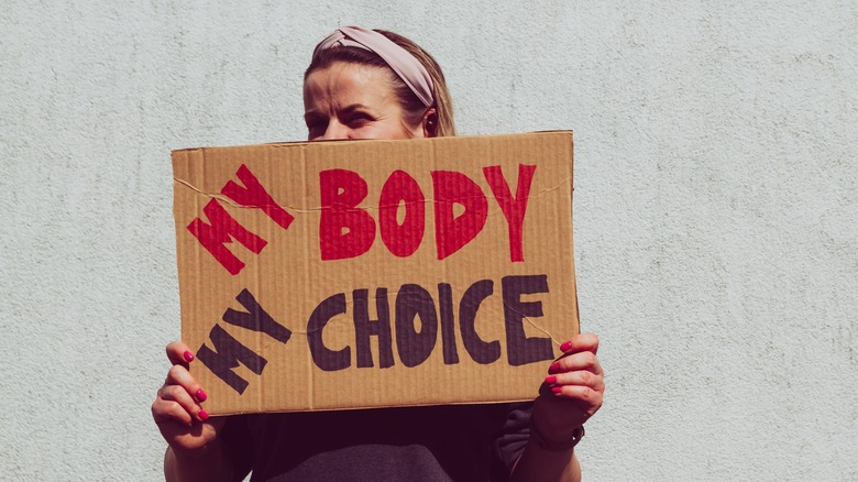 woman holding "my body my choice protest" pro abortion protest sign in front of her face