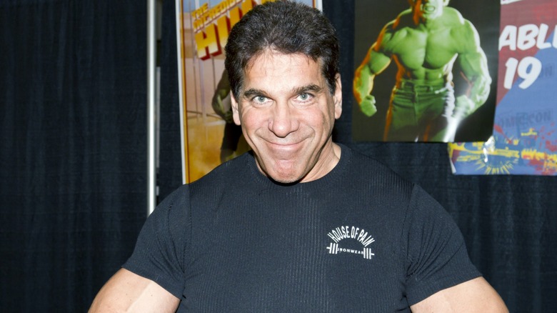 Lou Ferrigno smiling with Hulk poster behind him at Comic-Con