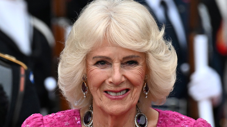 Queen Camilla smiling in a pink dress with dangly black diamond earrings
