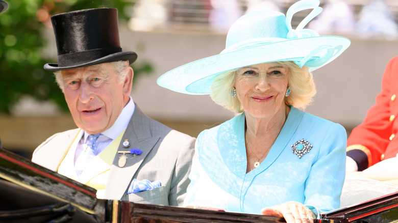 Charles in top hat and Camilla in blue dress and hat in open carriage for Ascot 2026