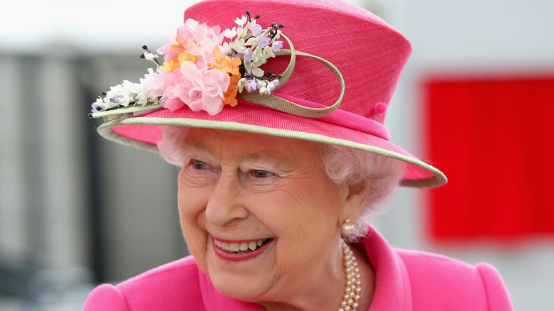 Queen Elizabeth smiling and wearing a pink hat