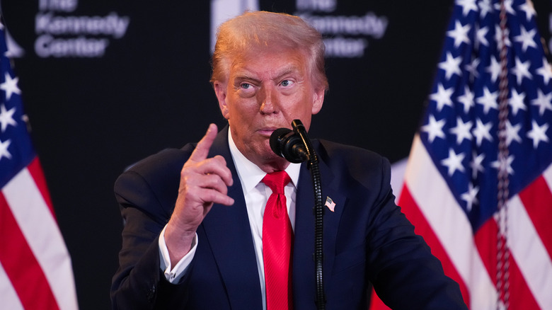 Donald Trump giving a speech in a navy suit with a red tie