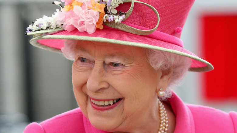 Queen Elizabeth smiling under a pink hat