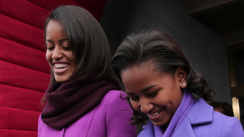 Malia and Sasha Obama smiling in purple jackets
