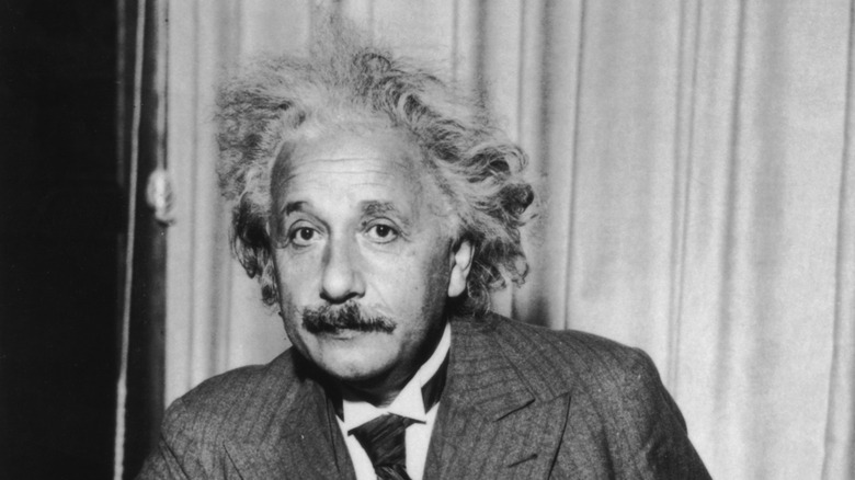 A black-and-white photo shows Albert Einstein looking directly into the camera lens