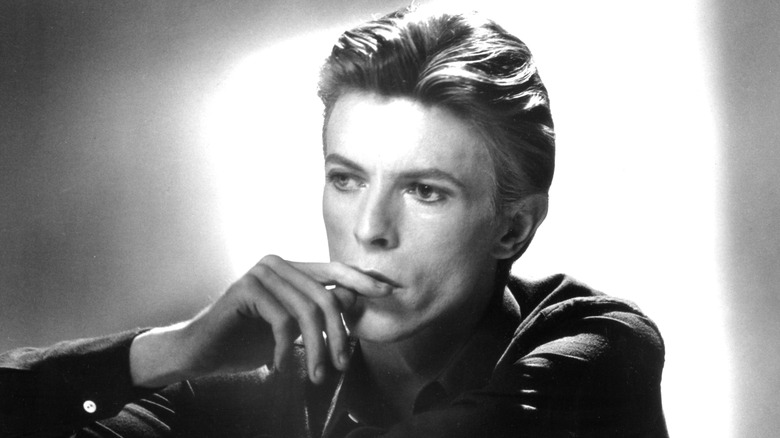 Black-and-white photo of David Bowie contemplatively looking off and touching his lip