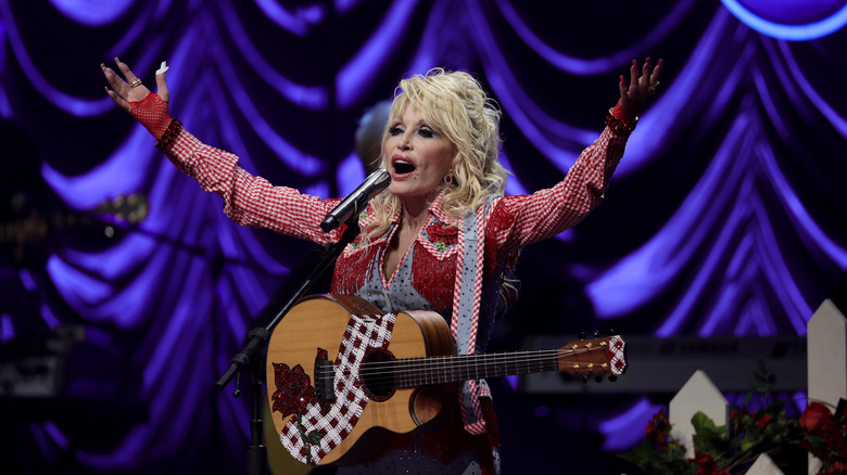 Dolly Parton singing and raising her arms in the air