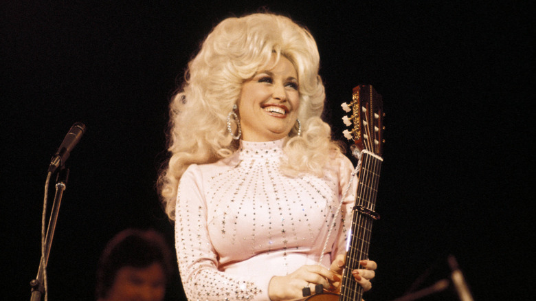 Dolly Parton holding a guitar and smiling onstage.