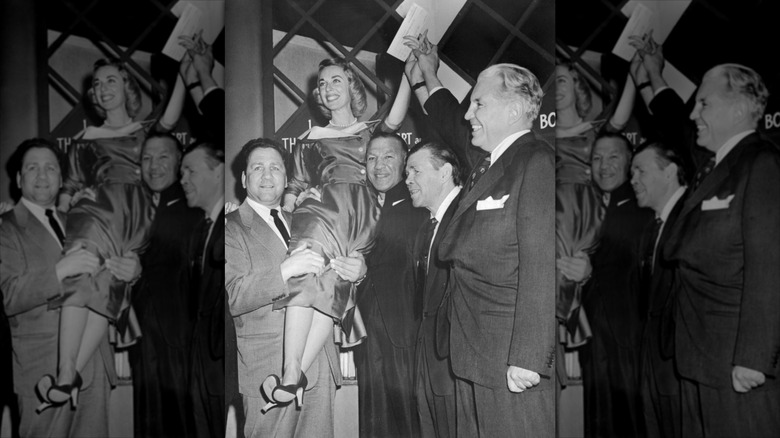Dr. Joyce Brothers holds up her winning check from "The $64,000 Question" while sitting on the shoulders of famous boxers and the show's host