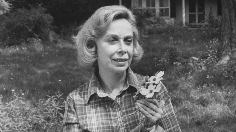 Dr. Joyce Brothers in flannel shirt holding some flowers in a garden and looking away from the camera