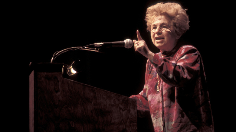 Dr. Ruth Westheimer talking into a microphone and pointing her finger