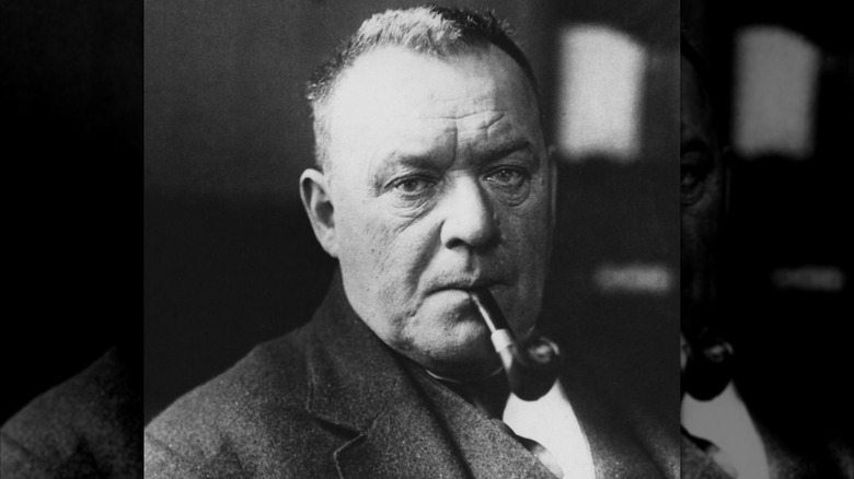 Hilaire Belloc looking serious and smoking a pipe
