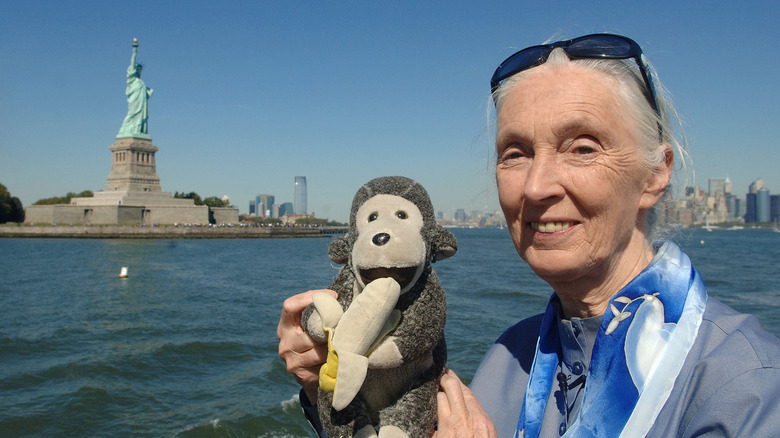 Jane Goodall holding a chimp stuffed animal on a boat with the Statue of Liberty in the background