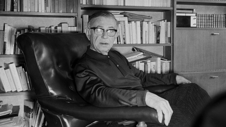 Jean-Paul Sartre sitting in a chair in front of bookshelves