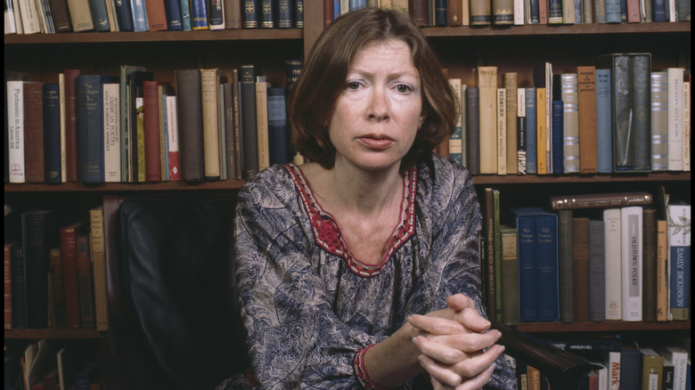 Joan Didion pictured in front of a stacked bookshelf
