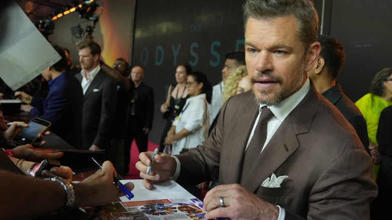 Matt Damon signing autographs on the red carpet wearing a brown suit