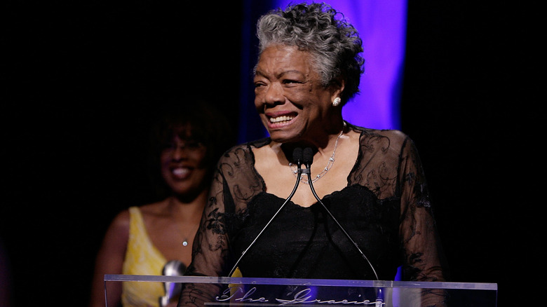 Maya Angelou smiling while delivering a speech in a black dress