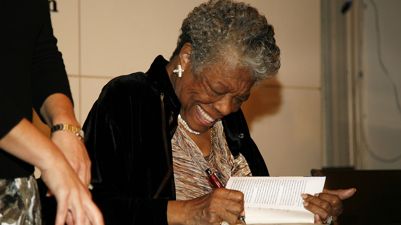 A beaming Maya Angelou smiling while signing a book
