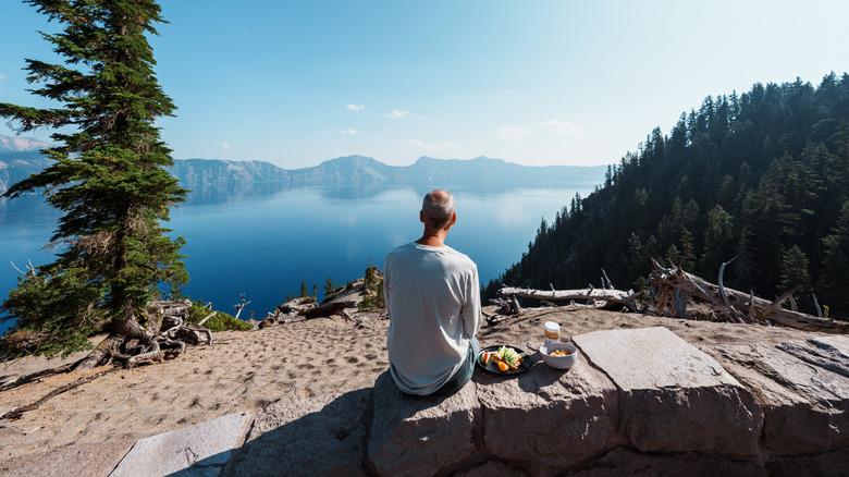 A photo of a man sitting on a stone block and enjoying the view of a lake