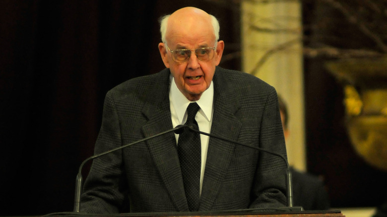 Wendell Berry speaking at a podium in a grey suit