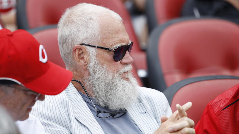 David Letterman watching a game in sunglasses and a stripy blazer