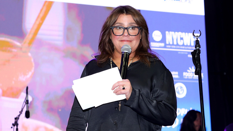 Rachael Ray holding a microphone and a piece of paper in a black shirt