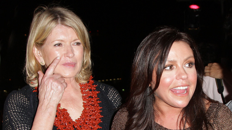 Rachael Ray speaking as she stands beside Martha Stewart touching her face