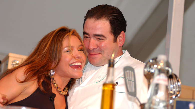 Rachael Ray laughing as she leans Emeril Lagasse in front of cookware