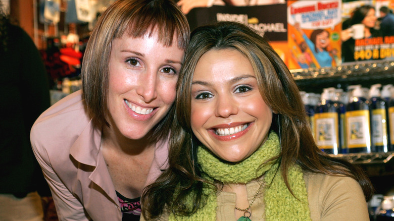 Rachael Ray smiling (R) with a guest (L) at a 2004 book signing, wearing a green shirt and scarf