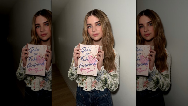 Raegan Revord holding a copy of her book in a darkened hall.