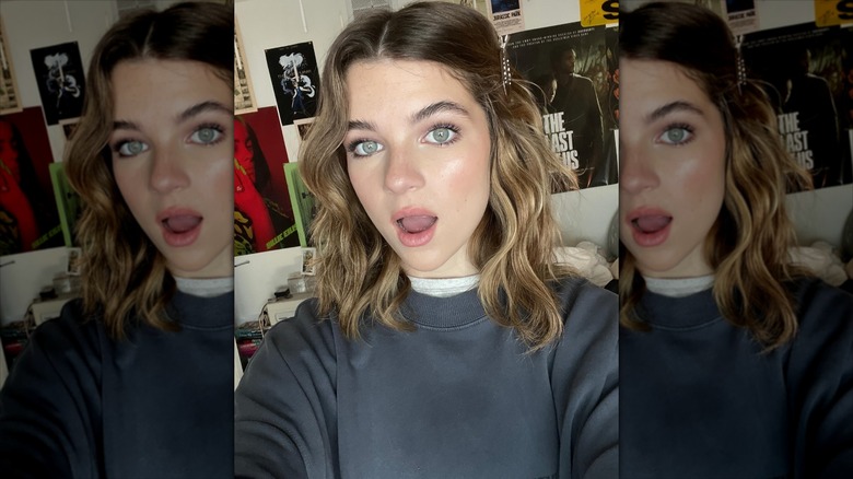 Raegan Revord with a shocked expression in a sweatshirt in front of posters.