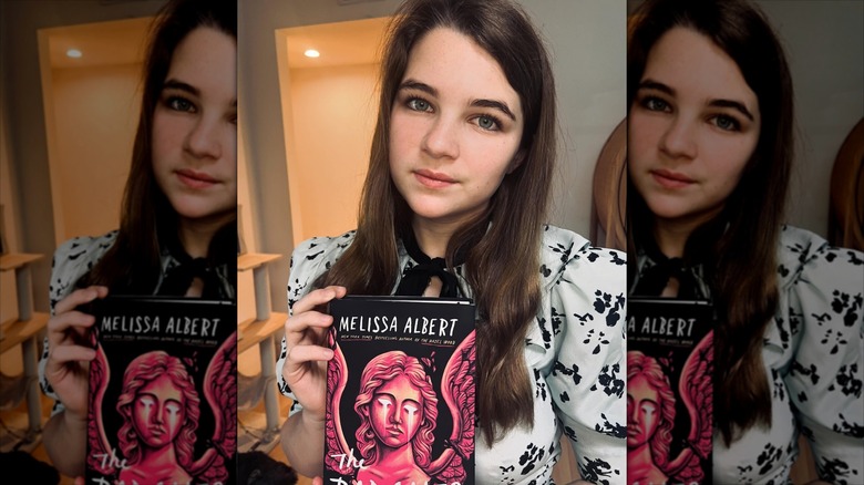 Raegan Revord poses with a book in a white and black dress.