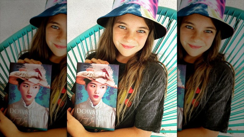 Raegan Revord wears a bucket hat while posing with a book.