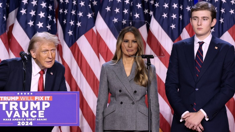 Donald Trump leaning forward at podium with Melania and Barron