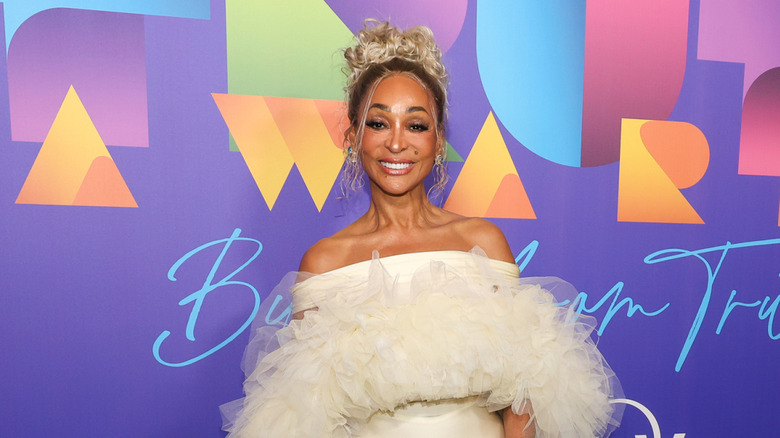 Karen Huger wearing an off-shoulder white dress with an up-do on the red carpet.