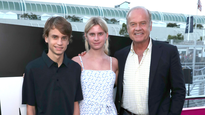 Kelsey Grammer smiles next to his children Mason and Jude standing outside with his arm around his daughter