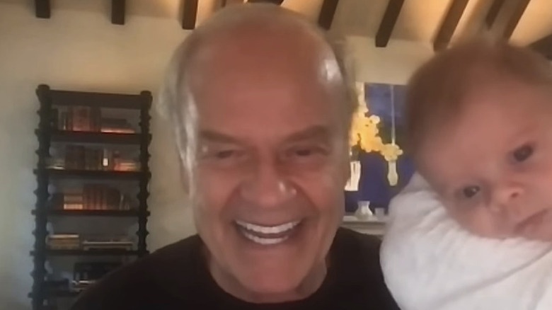 Kelsey Grammer smiles in front of a bookcase inside next to his baby son Christopher Grammer