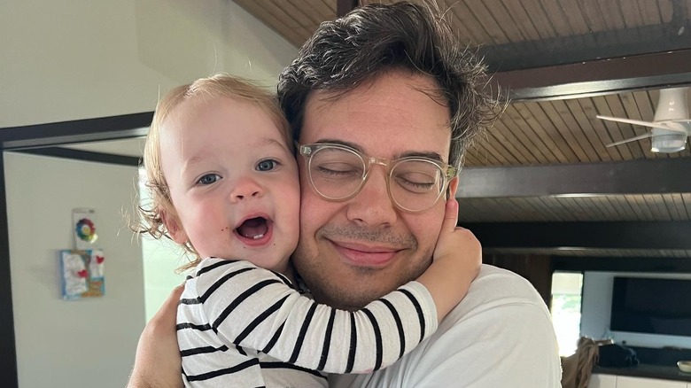 Nelson Franklin's child holds his neck smiling while Nelson smiles with his eyes closed