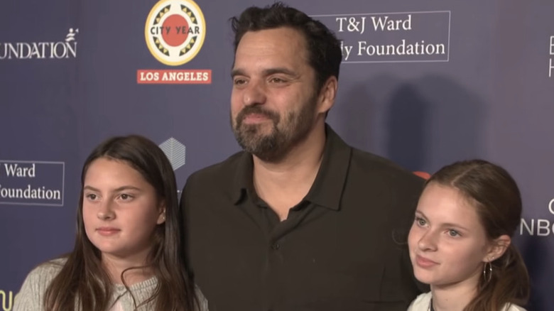 Jake Johnson from "New Girl" stands with his arms around his twin daughters on the red carpet