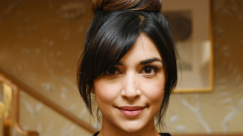 Hannah Simone from New Girl smiles against a tan wallpaper background