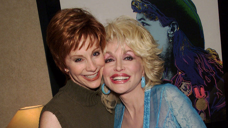 Dolly Parton and Reba McEntire hugging backstage at an event in 2001
