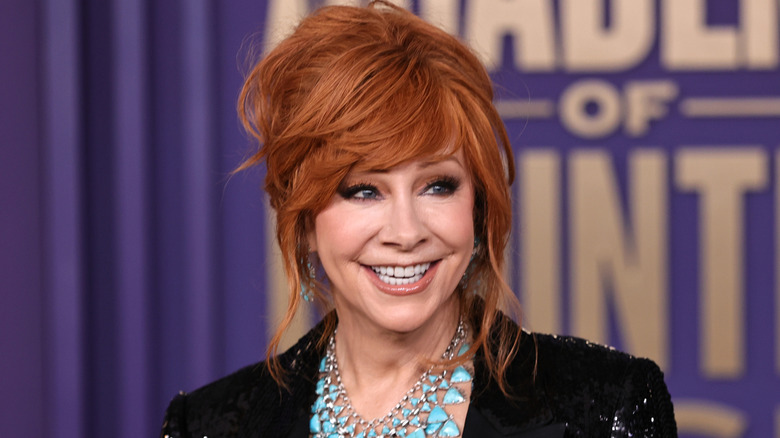 Reba McEntire smiling in a sparkly black blazer with her hair in an updo