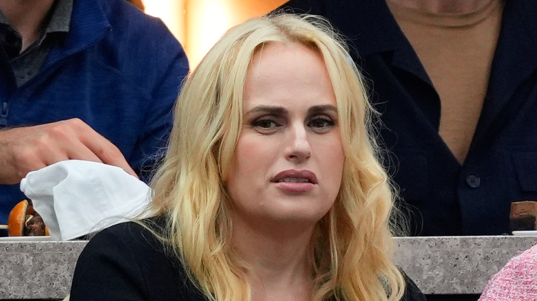 Rebel Wilson, in black, looking disgusted at a sporting event