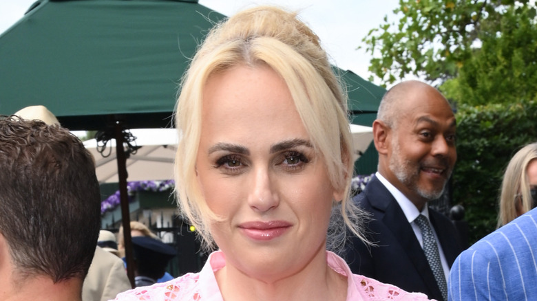 Rebel Wilson looking pretty in pink, with hair in updo, smiles at outdoor event